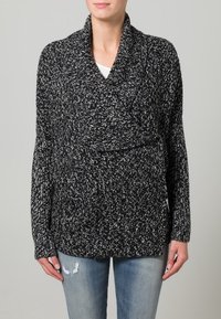 Pull en maille mouchetée noir et blanc avec col châle et manches longues, présentant une coupe décontractée et un tissu texturé.