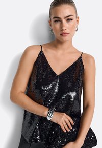 Čierny flitrový top na tenkých ramienkach s výstrihom do V. Skombinovaný s ladiacim flitrovým psaníčkom a strieborným náramkom.