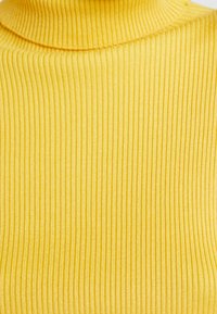 Maglione a collo alto giallo a coste realizzato in tessuto elasticizzato con righe verticali, caratterizzato da un colletto alto e una texture liscia.