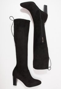 Stivali al ginocchio in suede nero con punta affusolata, chiusura con zip e un tacco a blocco spesso nero. Presentano un attacco a lacci nella parte superiore.