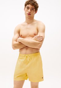 Shorts de bain jaunes en matériau léger, dotés d'une taille élastique avec cordon de serrage et d'un petit logo sur le côté.