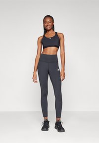 Soutien-gorge de sport noir et leggings taille haute gris foncé en tissu extensible. Présente un logo sur le soutien-gorge et des détails de couture subtils.