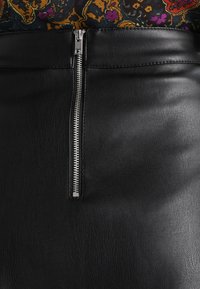 Jupe en cuir noir avec une fermeture éclair en argent bien visible à l'avant. Texture lisse avec un design ajusté. Couleur uniforme.