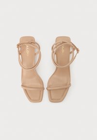 Sandales en cuir beige avec un design à bout carré, de fines brides de cheville et une silhouette minimaliste. Logo de la marque en or présent sur la semelle intérieure.