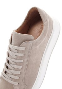 Sneaker in suede beige con punta arrotondata, dotato di lacci piatti, una suola in gomma bianca a profilo basso e un interno in pelle marrone liscia.