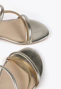 Metalliska guld sandaler i slät läder, öppen tå-design och tre tunna band, med en dekorativ dragkedjedetalj längs sidan.