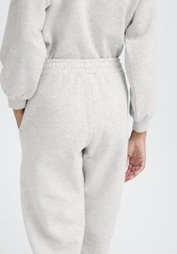 Sivé tepláky s elastickým pásom a bočnými vreckami, vyrobené z mäkkej, štruktúrovanej tkaniny. Pohľad zozadu ukazuje zúžený strih a jemný vzor látky.