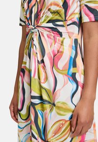 Sukienka w kwiatowy wzór z lekkiego materiału, w intensywnych kolorach, takich jak różowy, zielony i niebieski. Posiada węzeł przy talii.