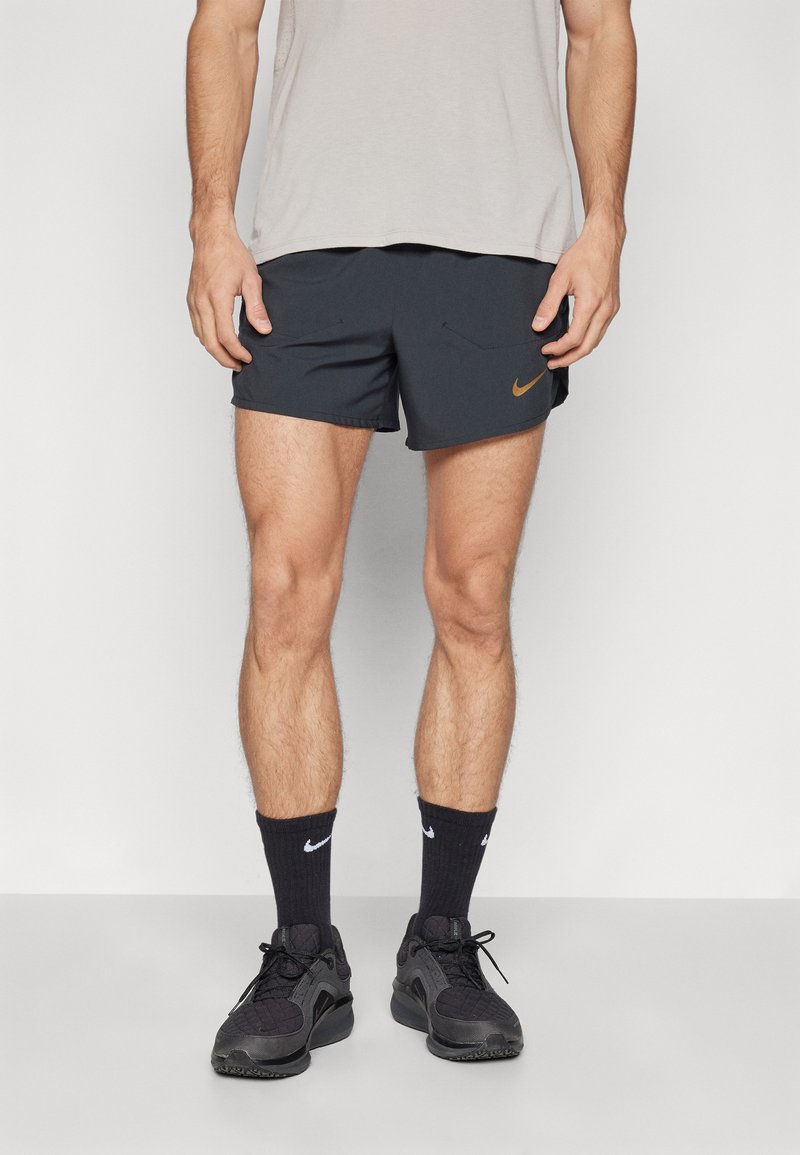 Svart sportshorts med oransje Nike-logo, kombinert med svarte sokker og joggesko. Avslappet passform; materialet virker lett og pustende.