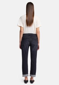 Jean en denim noir avec une coupe droite, des poignets retroussés et des coutures contrastantes. Associé à un t-shirt beige simple. Vue arrière montrée.