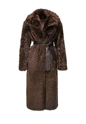 Femme portant un long manteau en fourrure marron texturé avec une ceinture noire, tenant un sac à main en fourrure imprimé léopard, des bas noirs et des talons noirs.