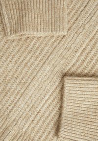 Stickad tröja i ljus beige med en strukturerad, ribbad mönstring och kontrasterande släta ärmar. Mjukt material med varierande stickningstekniker.