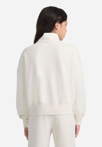 Krémový, voľný sveter s vysokým golierom, spustenými ramenami a rebrovanými manžetami. Mäkkučká, štruktúrovaná tkanina.