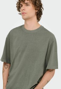 Oliven grøn bomulds T-shirt med korte ærmer, rund halsudskæring og afslappet pasform. Glat tekstur; ingen synlige mønstre eller hardware detaljer.