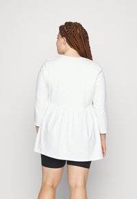 Camisola branca de manga longa com decote redondo e cintura franzida, feita de algodão macio. Combinada com calções pretos, apresentando um ajuste descontraído.