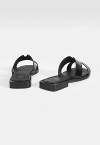 Zwarte platte sandalen met een stijlvolle, glanzende afwerking, open teenontwerp en kruislings gespen. De zool is plat en rechthoekig met een gestructureerde binnenzool.