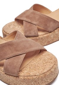 Braune Wildledersandalen mit Plateau und gekreuzten Riemen, die eine strukturierte Korksohle aufweisen. Das Design vereint Weichheit mit einem natürlichen Materialfinish.