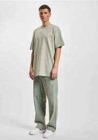Camiseta de gran tamaño de color verde claro, hecha de algodón suave, combinada con jeans sueltos de color verde claro y zapatillas blancas. Diseño simple y relajado.