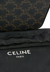 Pochette noire de créateur avec motif répétitif d'emblème marron reposant sur un tissu noir avec le logo blanc Celine Paris.