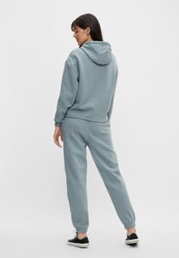 Hanorac albastru deschis și pantaloni jogger asortați din țesătură moale, cu glugă și manșete elastice, combinați cu adidași negri.