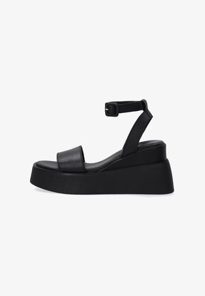 Sandales compensées en cuir noir avec bride à la cheville, présentant une large lanière sur les orteils et une semelle compensée texturée.