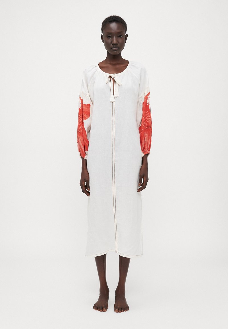 Weißes Leinenkleid mit langen, gepufften roten Ärmeln, die mit floralen Mustern verziert sind. Die Vorderseite hat einen Bindebandverschluss und ein zentrales Nahtdetail.