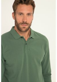 Dunkelgrünes Langarm-Polohemd aus Baumwolle mit einem Kragen und einer dreiknöpfigen Knopfleiste, das eine glatte, einfarbige Textur aufweist.