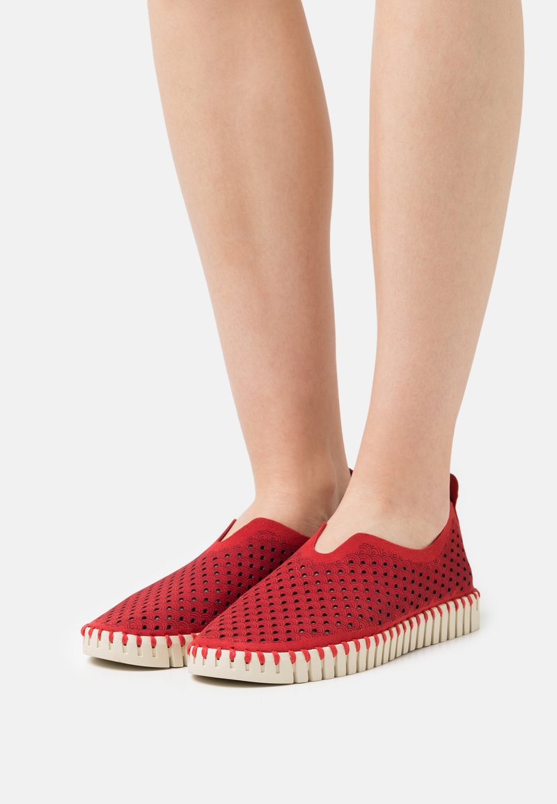Scarpe rosse slip-on con design superiore perforato, forma angolare e suola in gomma testurizzata con un motivo a zigzag bianco sul bordo.
