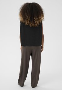 Musta sanslõikega särk, mis on lõdvalt istuv, koos hall-pruunide laia säärega pükstega, millel on tekstuuriga kangas ja mitteametlik kujundus.