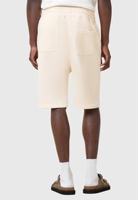 Pantaloni corti in felpa color crema con vita elasticizzata, due tasche posteriori e una texture liscia, pensati per cadere appena sopra il ginocchio.