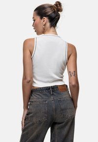 Biały dopasowany top na ramiączkach z wysokim dekoltem i kontrastowym przeszyciem, w połączeniu z ciemnoniebieskimi dżinsami z wysokim stanem i tylnymi kieszeniami.