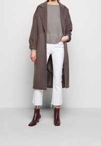Long manteau en laine marron avec de larges revers, porté sur un haut côtelé gris et un jean blanc court. Stylisé avec des bottines bordeaux.