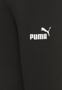 Fekete pamut leggings sima textúrával, fehér "PUMA" logóval és a bal comb felső részén található ugráló macskát ábrázoló emblémával.