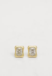Des boucles d'oreilles clou en métal doré avec une pierre claire à facettes carrée sertie dans un chaton à bords ondulés. Texture métallique lisse.