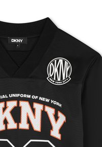 Maillot noir avec un design en V. Présente une texture en maille noire, un logo "DKNY" blanc et orange, ainsi qu'un patch circulaire DKNY NYC.