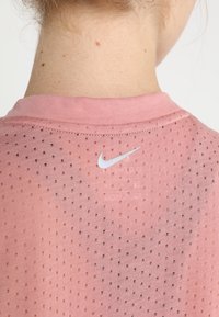 Roze ademende stoffen t-shirt met een gestructureerd patroon, voorzien van een klein wit Nike-logo aan de achterkant van de kraag.