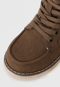 Braune Lederstiefel mit glatter Oberfläche, runder Spitze, dicken Schnürsenkeln, Metallösen und kontrastierenden Nähten auf einer Gummisohle.