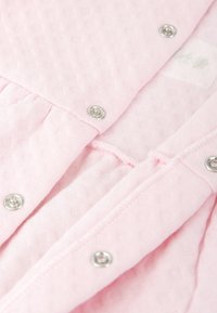 Tejido texturizado rosa con cierres a presión plateados; presenta un diseño fruncido y un material suave y ligero para mayor comodidad y facilidad de uso.