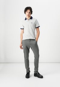 Striped polo shirt with navy collar, worn with gray jogger pants, complemented by black shoes. Smooth fabric and casual fit.