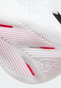 Semelle de chaussure blanche avec motif de bande de roulement en zigzag, agrémentée d'accents rouges. Adhérence texturée avec des profondeurs variées et des bords lisses et arrondis.