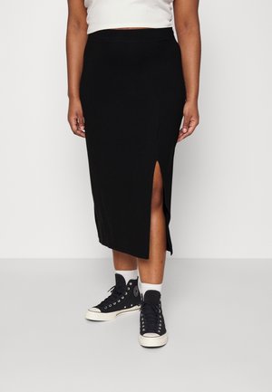 Jupe noire tricotée avec une fente sur le côté, taille ajustée et texture lisse. Assortie à des baskets noires montantes et des chaussettes blanches mi-mollet.