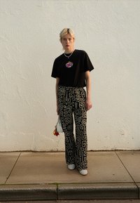 Μαύρο κοντομάνικο φανελάκι με πολύχρωμο σχέδιο, συνδυασμένο με ψηλόμεσα μαύρα και λευκά παντελόνια με μοτίβο και λευκά παπούτσια. Μικρή τσάντα χειρός.