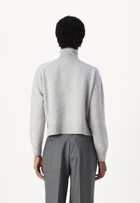 Grauer kurz geschnittener Pullover mit hohem Kragen und geripptem Saum. Der Stoff wirkt weich mit einer strukturierten Oberfläche, kombiniert mit grauen, maßgeschneiderten Hosen.