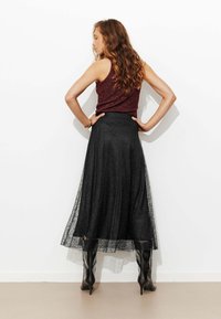 Jupe longue en dentelle noire superposée à un tissu noir uni, associée à un haut sans manches bordeaux et des bottes noires à talons montant jusqu'aux genoux.