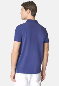 Polo shirt blu navy in cotone, con colletto classico e maniche corte, dotato di spacchi laterali e discreta marca sull'orlo.