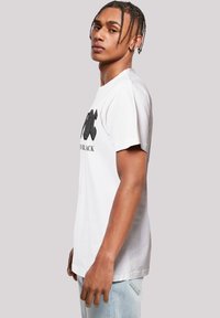White cotton t-shirt featuring a bold black graphic design across the chest, short sleeves, and a relaxed fit. Minimalist style overall.
