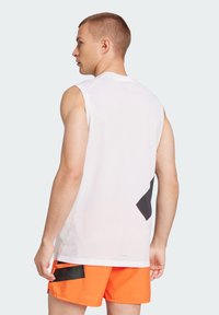 White sleeveless athletic shirt with mesh fabric, featuring black geometric accents. Worn with orange shorts, showing a sporty design.