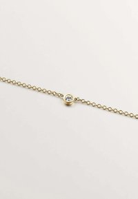 Pulsera de cadena de oro con una sola piedra preciosa redonda y clara engastada en un soporte circular, con un diseño de cadena delicado.