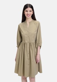 Khakifarbendes Hemdblusenkleid mit einer durchgehenden Knopfleiste, Stehkragen und dreiviertellangen Puffärmeln; geraffte Taille und glatte Textur.