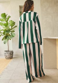 Ensemble en deux pièces avec des rayures verticales vertes et blanches ; comprend une chemise à col et un pantalon large en tissu doux et lisse.